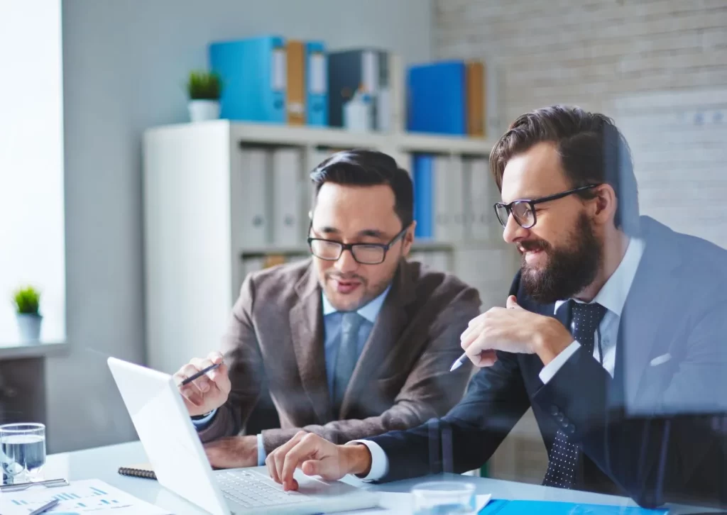 "Two professional business consultants discussing work on a laptop in a modern office environment.