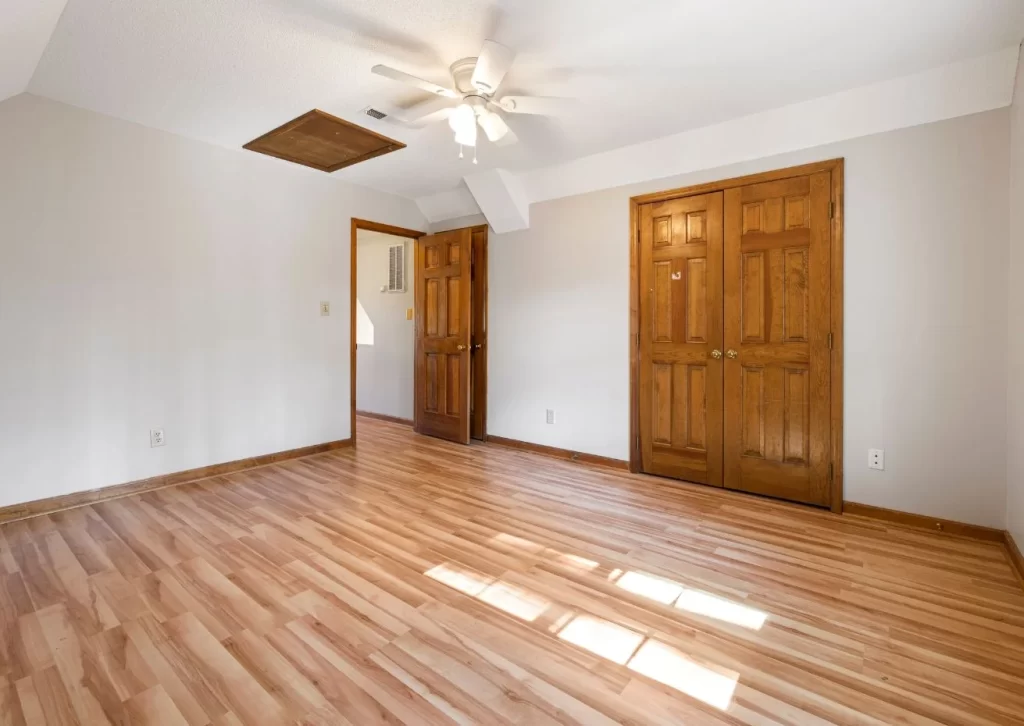 Bright empty room with polished laminate flooring, wooden doors, and natural light creating a warm and inviting space.